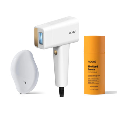 Nood Flasher Pro Kit in white including white Eraser exfoliating tool, Flasher Pro IPL device in white with gold accents, and Nood Serum daily aftercare on white background